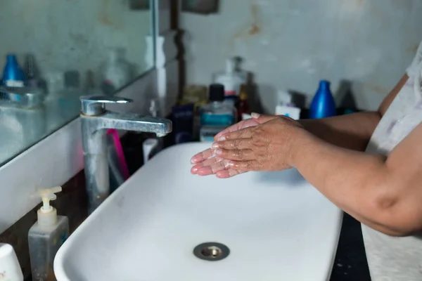 Yetişkin bir kadın, Coronavirus 'la savaşmak için lavabonun ve lavabonun altındaki sabunla ellerini ve kollarını düzgün bir şekilde yıkıyor. Banyo konsolu, arka planda bir sürü ürünle el yıkama, metin eklemek için yer