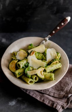 Kabaklı yeşil makarna ve gri bir yüzeyde parmesan peyniri..