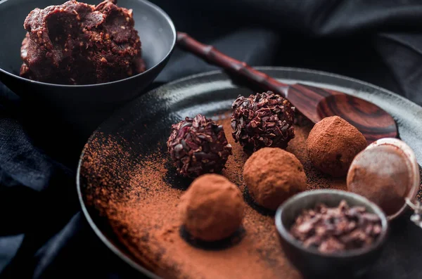 Date energy ball with cocoa on a black dish and cocoa nibs.