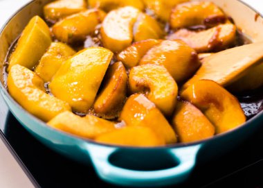 Mavi saplı ve mavi spatulalı dökme demir bir tavada karamelize edilmiş elma..