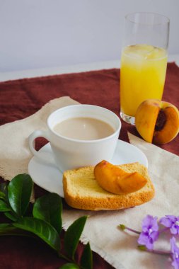 Bir fincan tostlu kahve, şeftali suyu ve kırmızı arka planda yapraklar