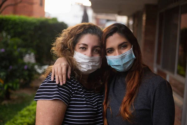 Latin anne ve kızı birbirlerine maskeyle sarılıyorlar.
