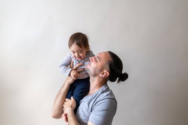 Genç, uzun saçlı bir baba kızını omzunda taşıyor. Beyaz stüdyo arka planında yakalandı