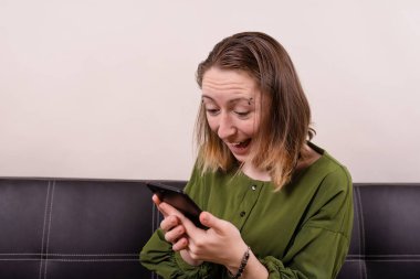 Yeşil elbiseli mutlu kadın ellerinde telefonla duygusal bir şekilde bakıyor.