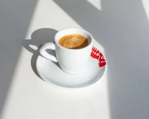 窓から影が付いている朝の赤いプリントの白いカップの中のエスプレッソ — ストック写真