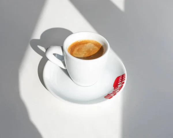 Espresso in a white cup with a red print in the morning with shadows from the window