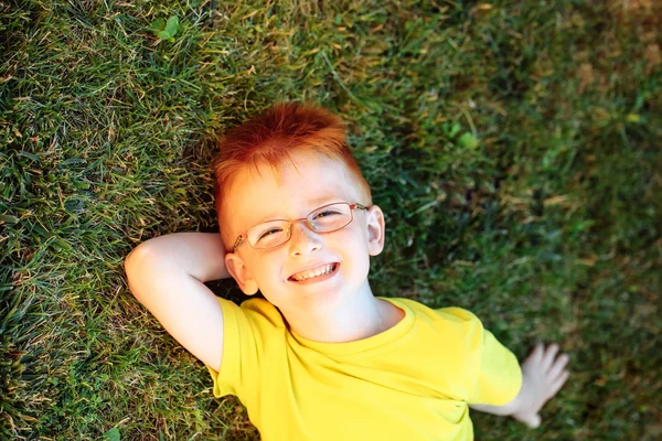 Happy babyjongen met rood haar in glazen op gras — Stockfoto