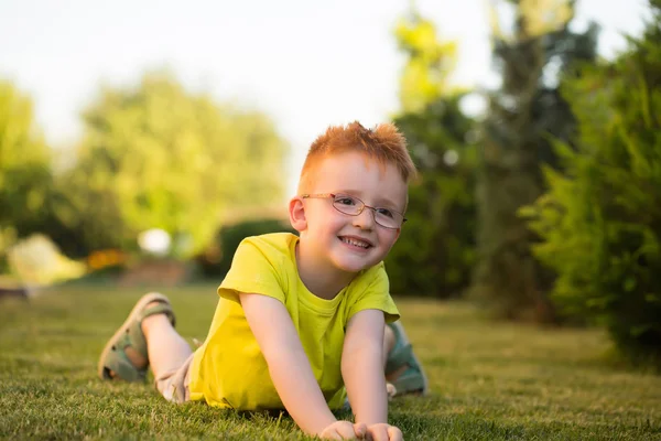 Счастливый мальчик с рыжими волосами в очках на траве — стоковое фото
