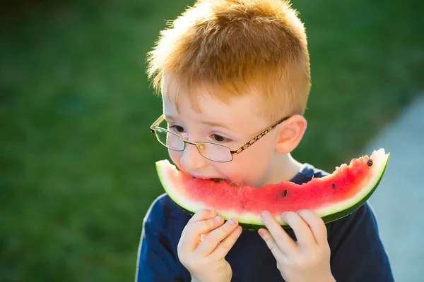 Menino feliz com cabelo vermelho em óculos comendo melancia — Fotografia de Stock