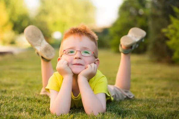 Babyjongen met rood haar in glazen op gras — Stockfoto