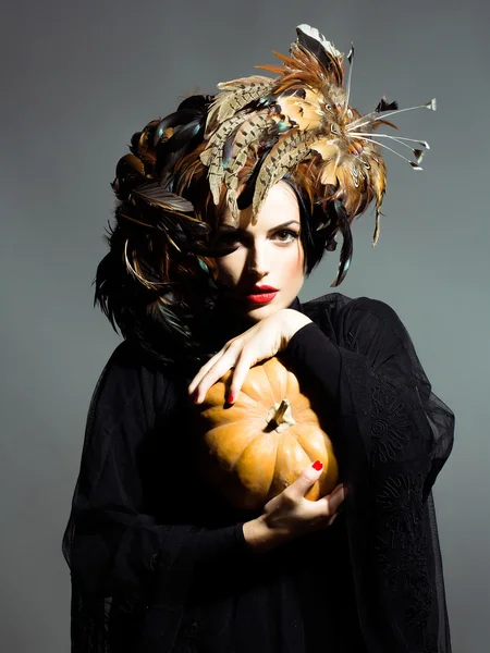 Jolie femme en plumes chapeau tient halloween citrouille — Photo