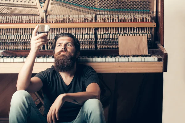 Homme barbu avec verre près du piano en bois — Photo