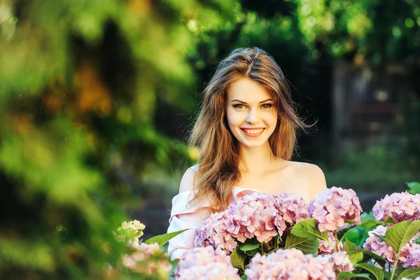 Bonita chica sonriente en hortensias flores — Foto de Stock