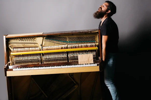 Homem barbudo tentando mover piano de madeira — Fotografia de Stock