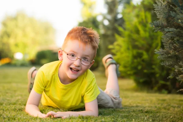 Lycklig pojke med rött hår i glas på gräs — Stockfoto