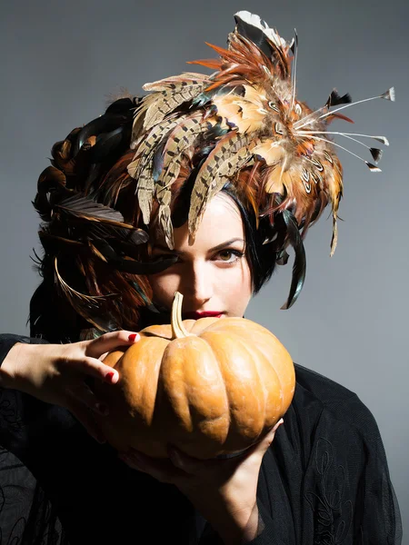 Bonita mujer en sombrero de plumas sostiene la calabaza de Halloween —  Fotos de Stock