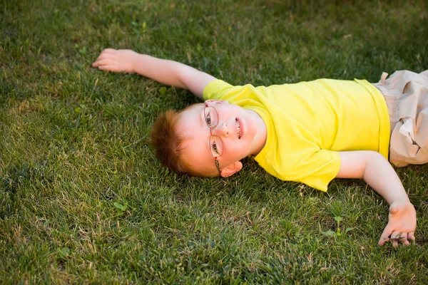 Niño feliz con el pelo rojo en gafas en la hierba — Foto de Stock