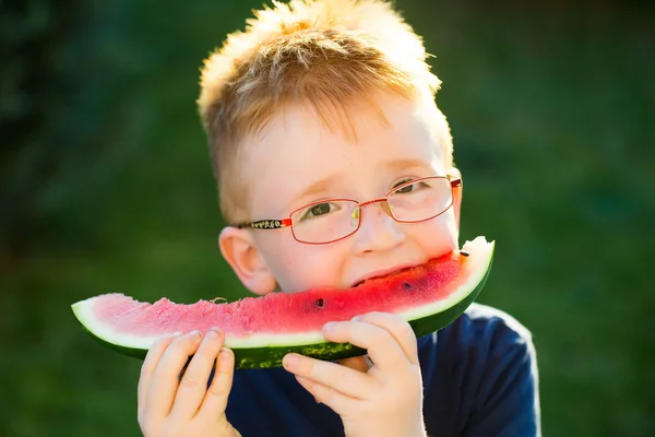 Niño feliz con el pelo rojo en gafas comiendo sandía — Foto de Stock