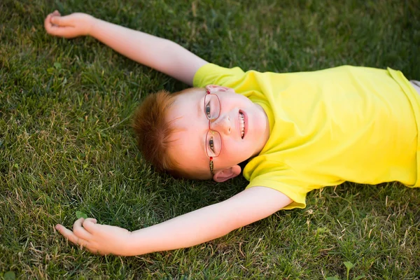 Glücklicher kleiner Junge mit roten Haaren in Brille auf Gras — Stockfoto