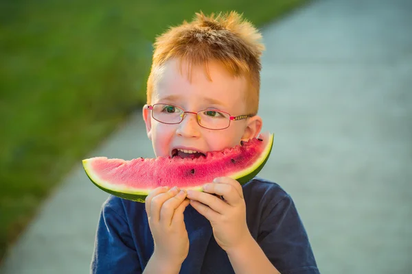 Niño feliz con el pelo rojo en gafas comiendo sandía —  Fotos de Stock