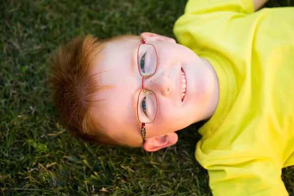 Menino feliz com cabelo vermelho em óculos na grama — Fotografia de Stock
