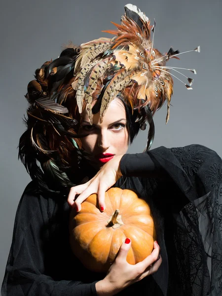 Bonita mujer en sombrero de plumas sostiene la calabaza de Halloween —  Fotos de Stock