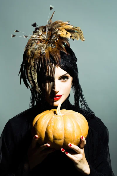 pretty sexy woman in feather hat holds pumpkin