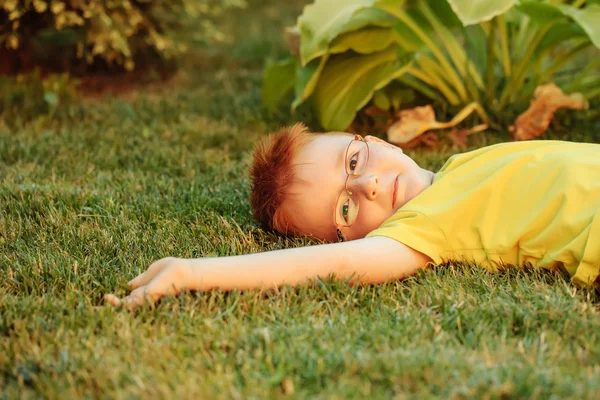 Lycklig pojke med rött hår i glas på gräs — Stockfoto
