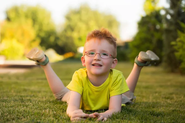 Happy babyjongen met rood haar in glazen op gras — Stockfoto