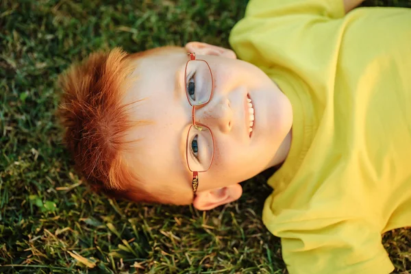 Bambino felice con i capelli rossi negli occhiali sull'erba — Foto Stock