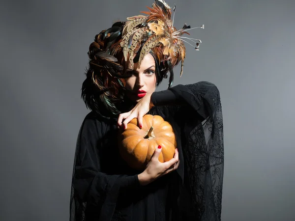 Mulher bonita em chapéu de penas detém abóbora halloween — Fotografia de Stock