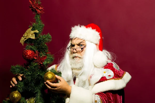Serious santa decorates Christmas tree — Stock Photo, Image