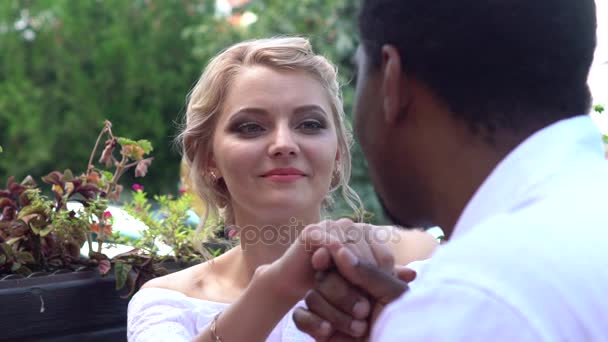 Доблестный черный мужчина заботится о белой девушке, целует руку свидания в кафе — стоковое видео