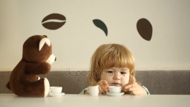 Дети играют с плюшевым мишкой и пьют с ним кофе с молоком в кафе — стоковое видео