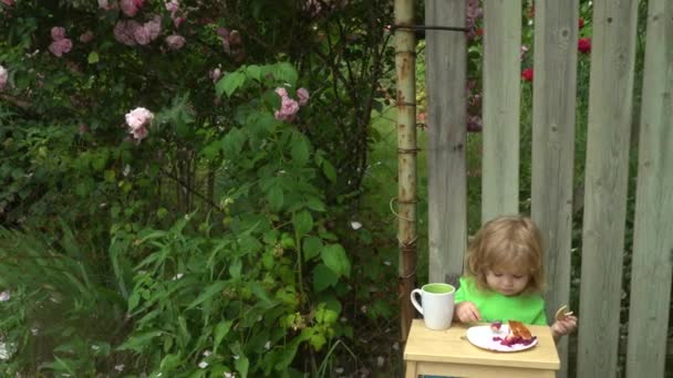 Mooie baby in de tuin eten taart met kersen — Stockvideo