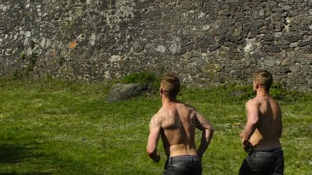 Dois atletas correndo por aí com um tronco nu perto das paredes medievais — Vídeo de Stock
