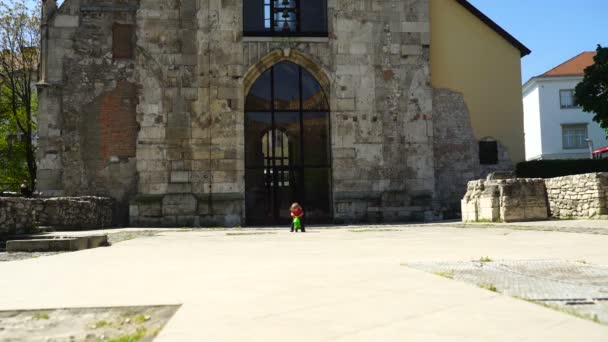 Menino vai para uma unidade em uma bicicleta infantil no centro da cidade velha perto da igreja — Vídeo de Stock