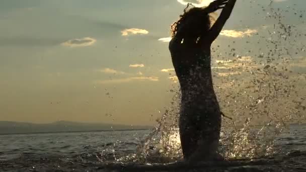 MOCIÓN LENTA: Chica jugando con salpicaduras en aguas poco profundas al atardecer — Vídeo de stock