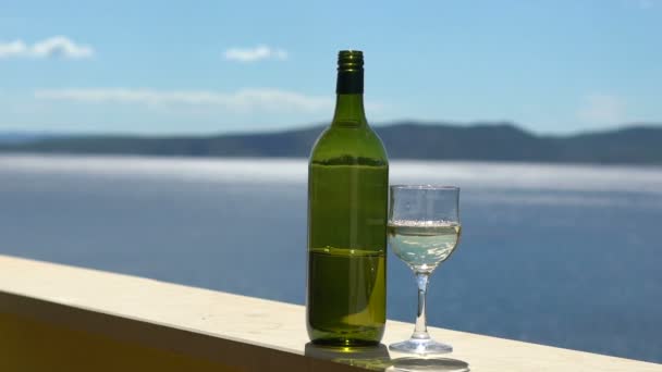 Бутылка и стакан белого вина на фоне солнечного дня в море, замедленная съемка — стоковое видео