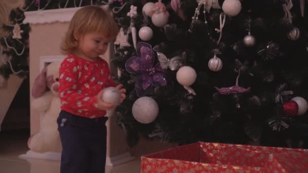 Симпатичный ребенок сбрасывает шарики с елки в коробку — стоковое видео