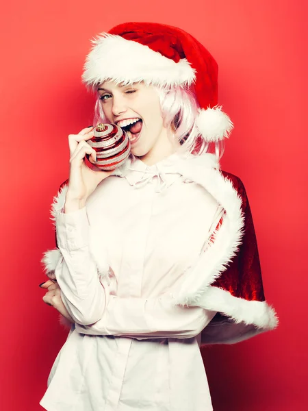 Подмигивающая девушка кусает рождественскую безделушку — стоковое фото