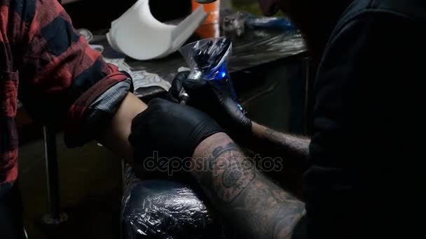 Master tatuering ritar på klienter tatueringen. Professionell konstnär håller en svart tatueringsmaskin i svart sterila handskar och arbetar, gör en tatuering på en manlig hand — Stockvideo