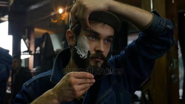 Красивий чоловік голиться в перукарні з піною і ручною небезпечною бритвою. Молодий перукар голиться сам — стокове відео