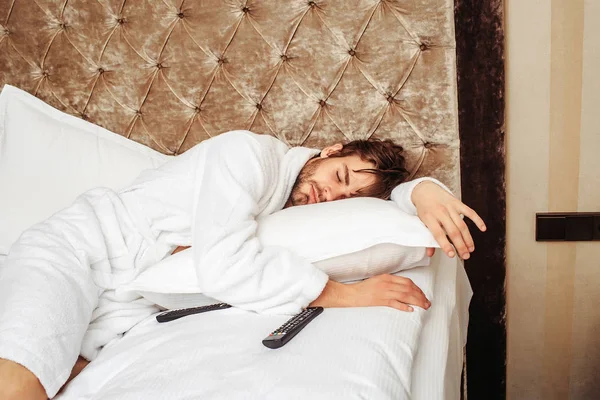 Szakállas férfi ágy távirányítóval — Stock Fotó