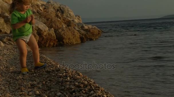 Niños jugando con piedras en la playa al atardecer cerca del mar. Fondo de niños. Niño de vacaciones — Vídeo de stock