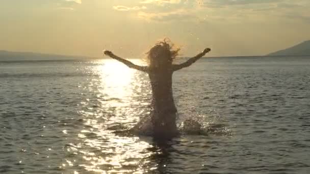 Zwolnionym tempie: szczęśliwy dziewczyna gra z wody na letnie wakacje morze lub ocean. Dziewczyna sprawia, że rozpryski wody na tle zachodu słońca — Wideo stockowe