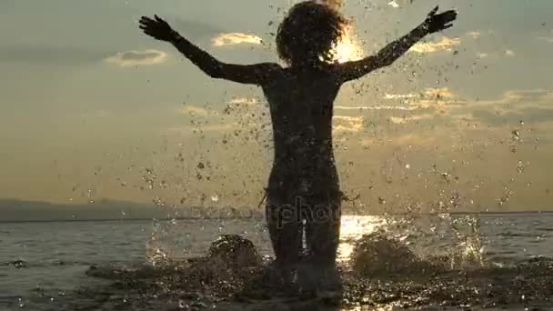 Menina sexy ao pôr do sol pulando na água. Mulher magra fazendo salpicos com água. Viaje de férias no mar em férias. Movimento lento — Vídeo de Stock