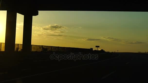 スローモーション: 夕暮れ時橋の下で高速道路。夕方の空の背景上のトラフィックと長い道のりと夕日 — ストック動画