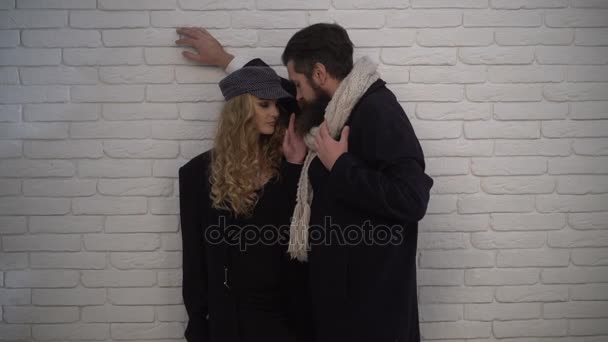Hombre abrazando a mujer rizada cerca de una pared de ladrillo blanco. Cita rubia y morena, cita con un hombre barbudo que lleva una bufanda — Vídeos de Stock