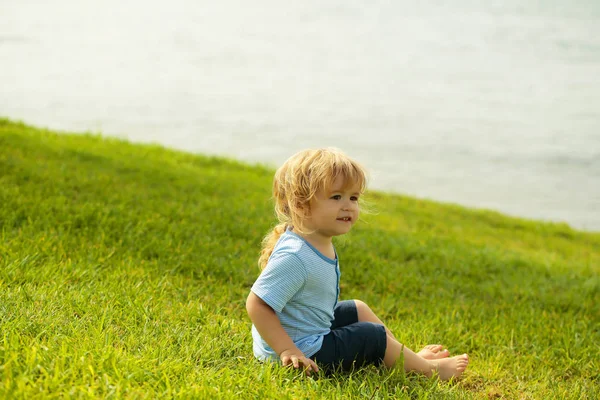 Aranyos kisfiú ül a zöld fű — Stock Fotó